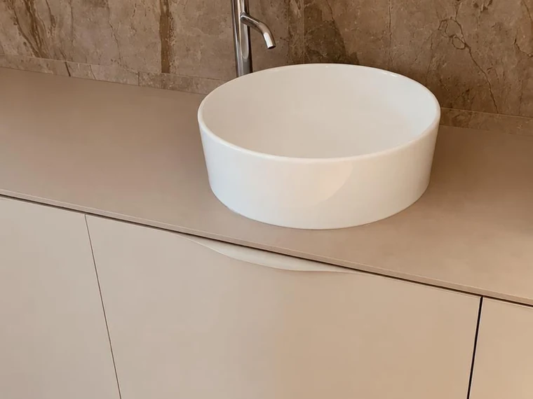 Vasque à poser ronde sur un plan de toilette en pierre, meubles blancs et parquet
